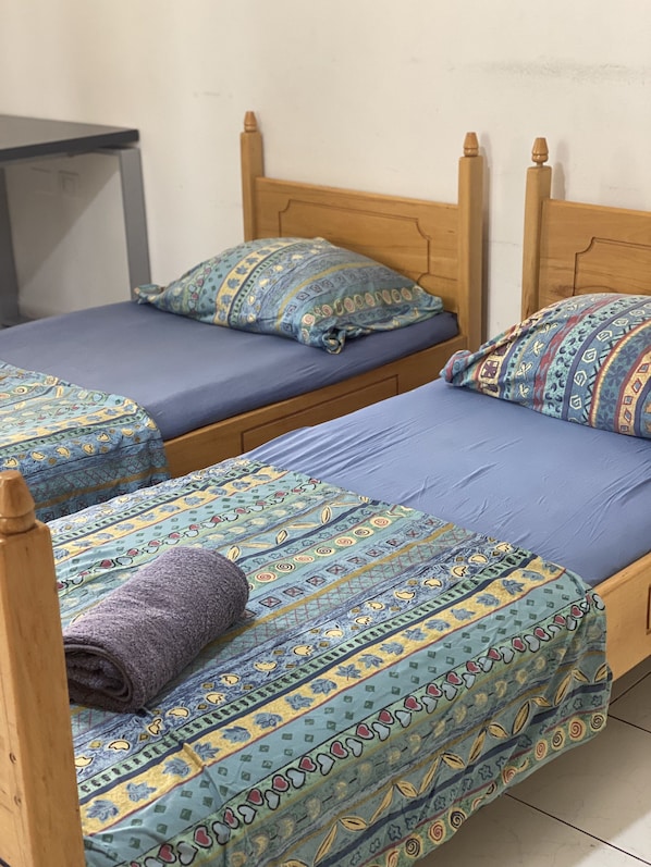Two wooden beds with blue bedding and patterned pillows, a small table, and a plain wall.