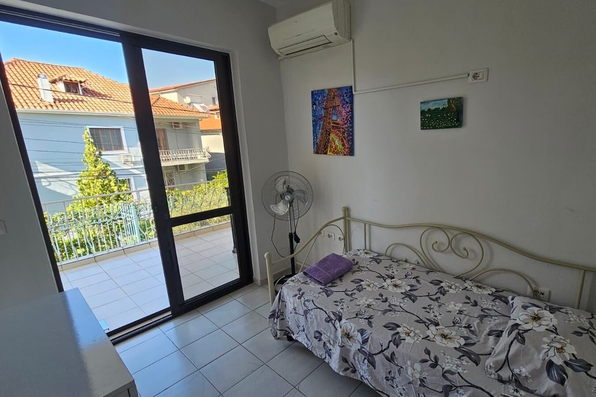 Une chambre à coucher avec un lit, un ventilateur, une fenêtre et un balcon.