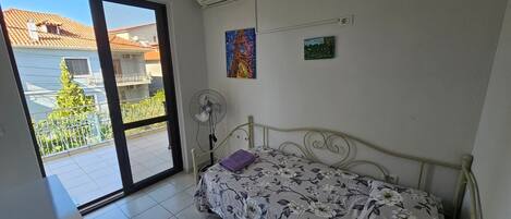 A bedroom with a bed, a fan, a window, and a balcony.
