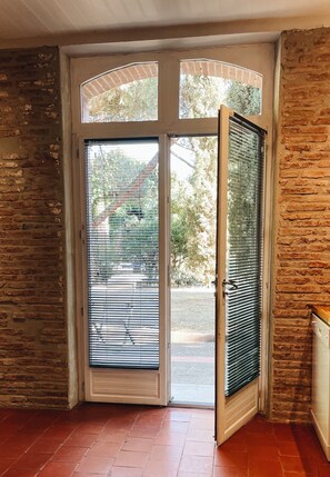Una habitación con pared de ladrillo, una puerta con panel de vidrio y vista al exterior.