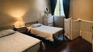 Un dormitorio con dos camas, un aparador, un espejo, una ventana con cortinas y un radiador.
