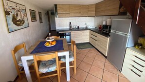 A compact kitchen with wooden cabinets, a dining table with chairs, a refrigerator, and a tiled floor. - Apartment in Residence Marina di Pinarello (Zonza)