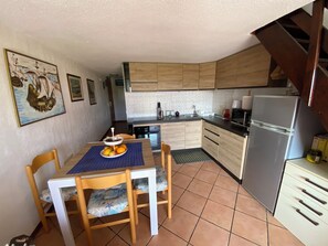 Uma cozinha compacta com armários de madeira, uma mesa de jantar com cadeiras, uma geladeira e piso de azulejos.