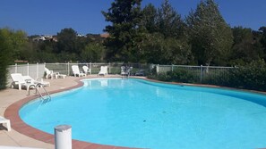 Une piscine entourée de chaises longues blanches et d’une clôture en métal.