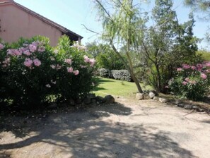 Uma entrada de cascalho leva a uma casa com arbustos de flores cor-de-rosa.