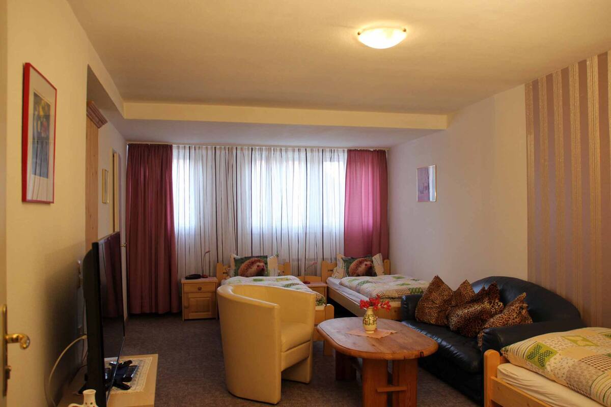 A hotel room with two beds, a sofa, a TV, and a desk.