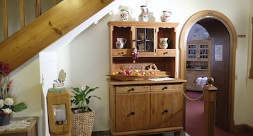 Um armário de madeira com portas de vidro, uma pequena mesa com um vaso de flores e uma planta numa cesta de vime.