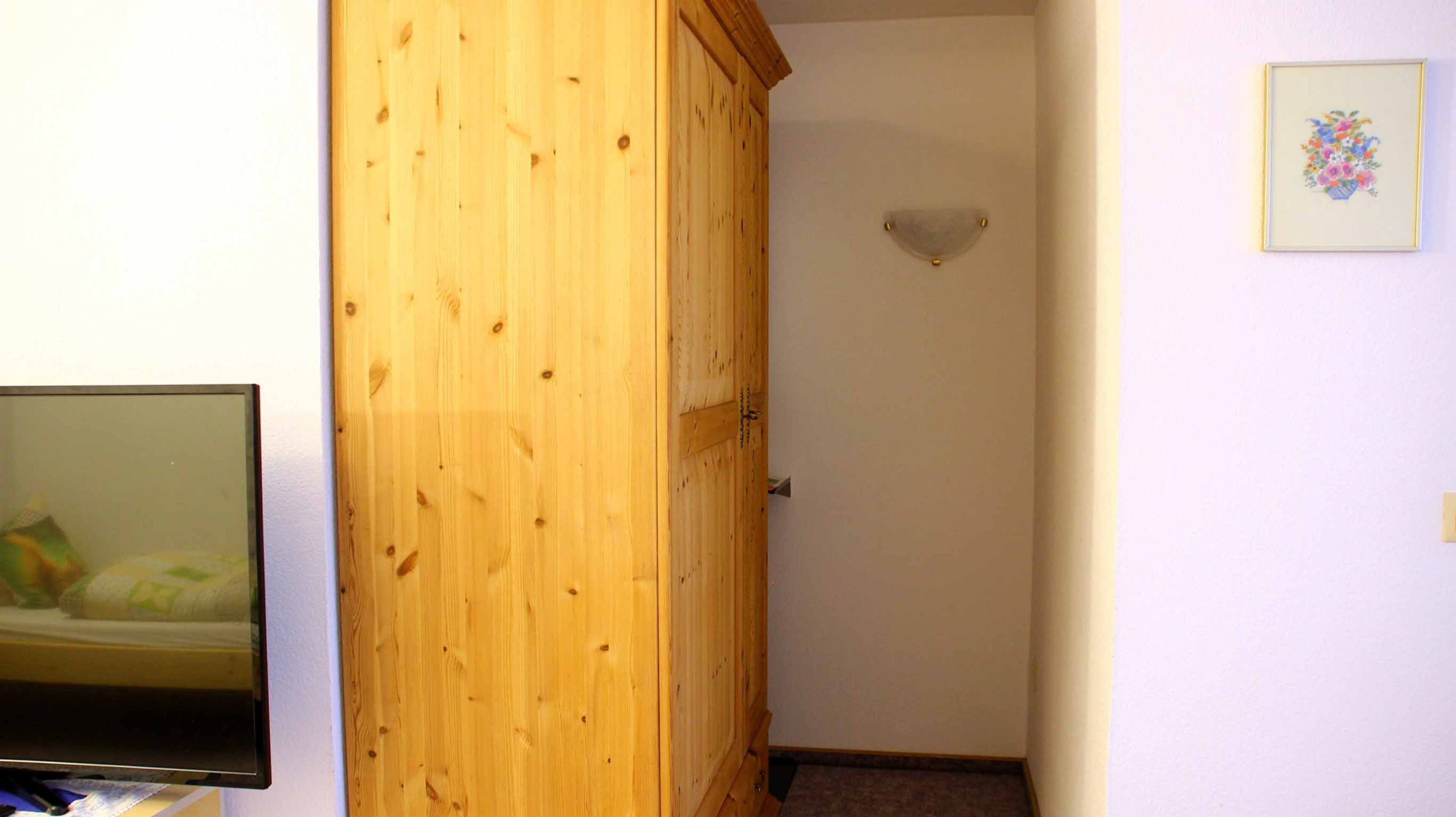 A hallway with a wooden door, a wall-mounted light fixture, and a framed picture.