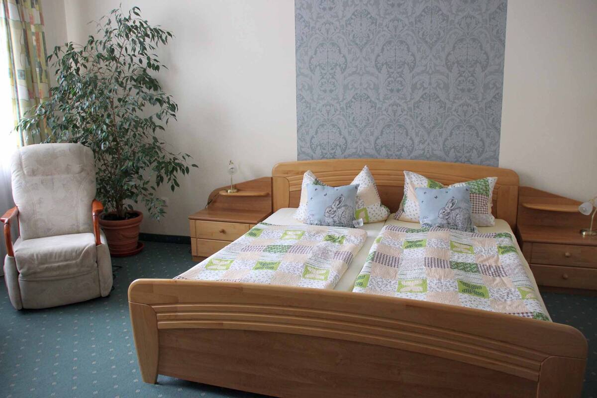 A bedroom with a wooden bed, two nightstands, a chair, and a potted plant.