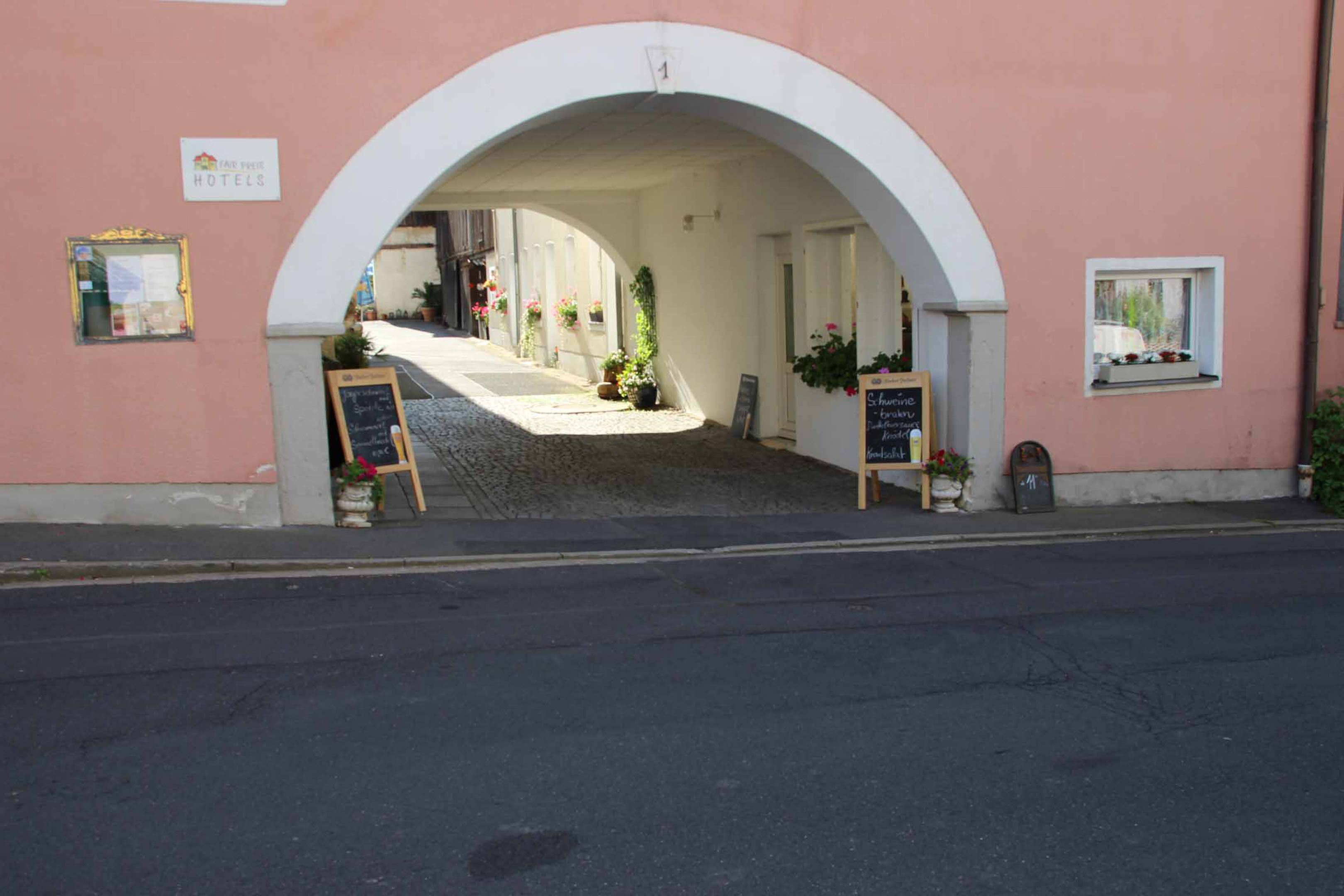 A hotel entrance with an arched doorway, a signboard, and potted plants.