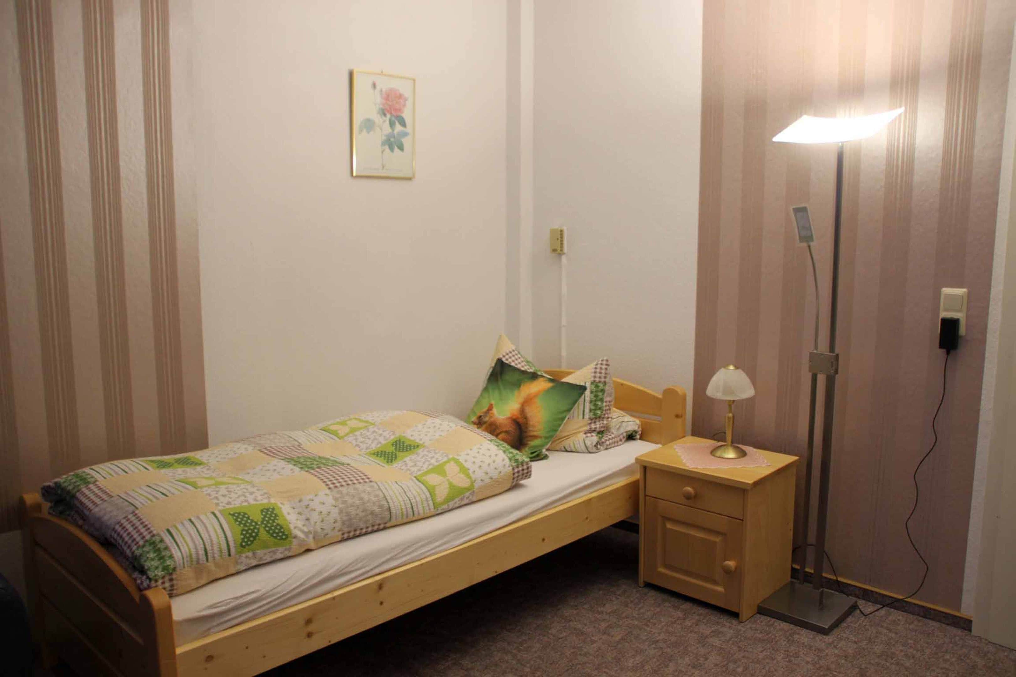 A small, neatly made bed with a quilt, a bedside lamp, and a nightstand with a drawer.