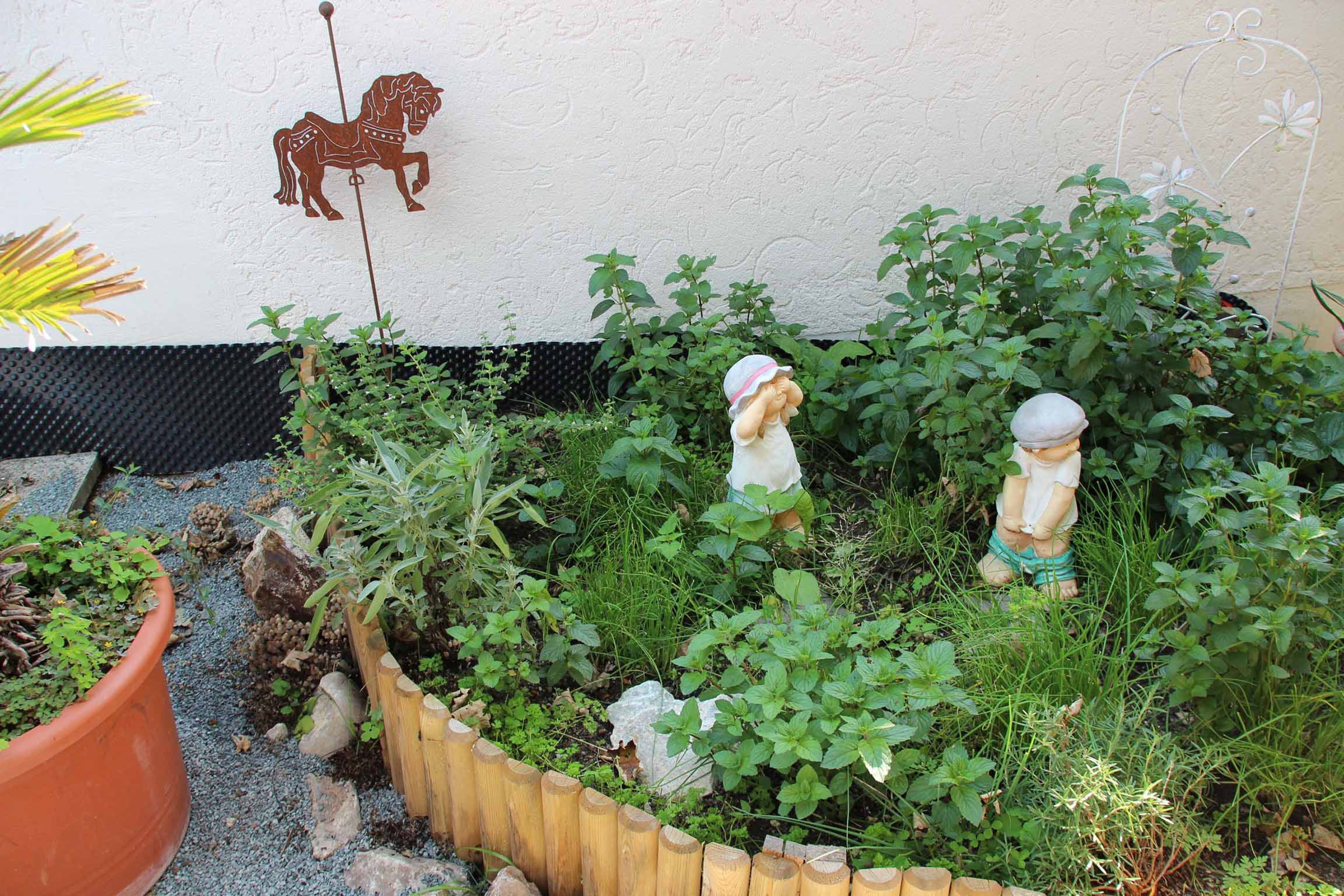 Un jardín con cerca de madera, una decoración de caballo y dos figuritas.