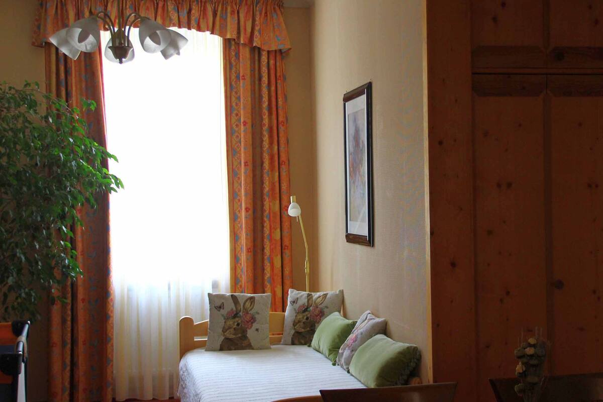 A room with a bed, a window with curtains, a wall-mounted picture, and a door leading to a bathroom.