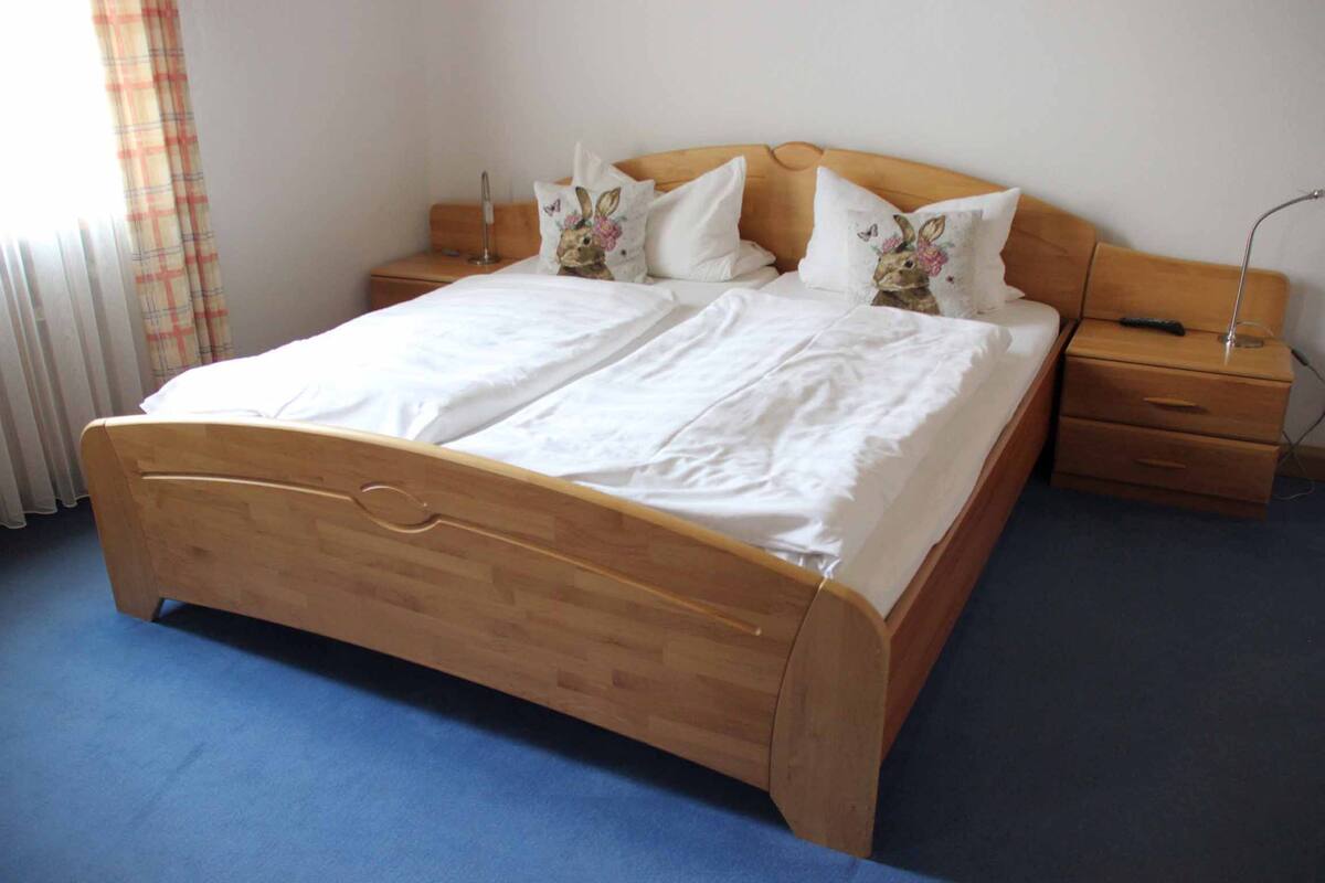 A double bed with a wooden frame, two bedside tables, and a nightstand with a lamp.