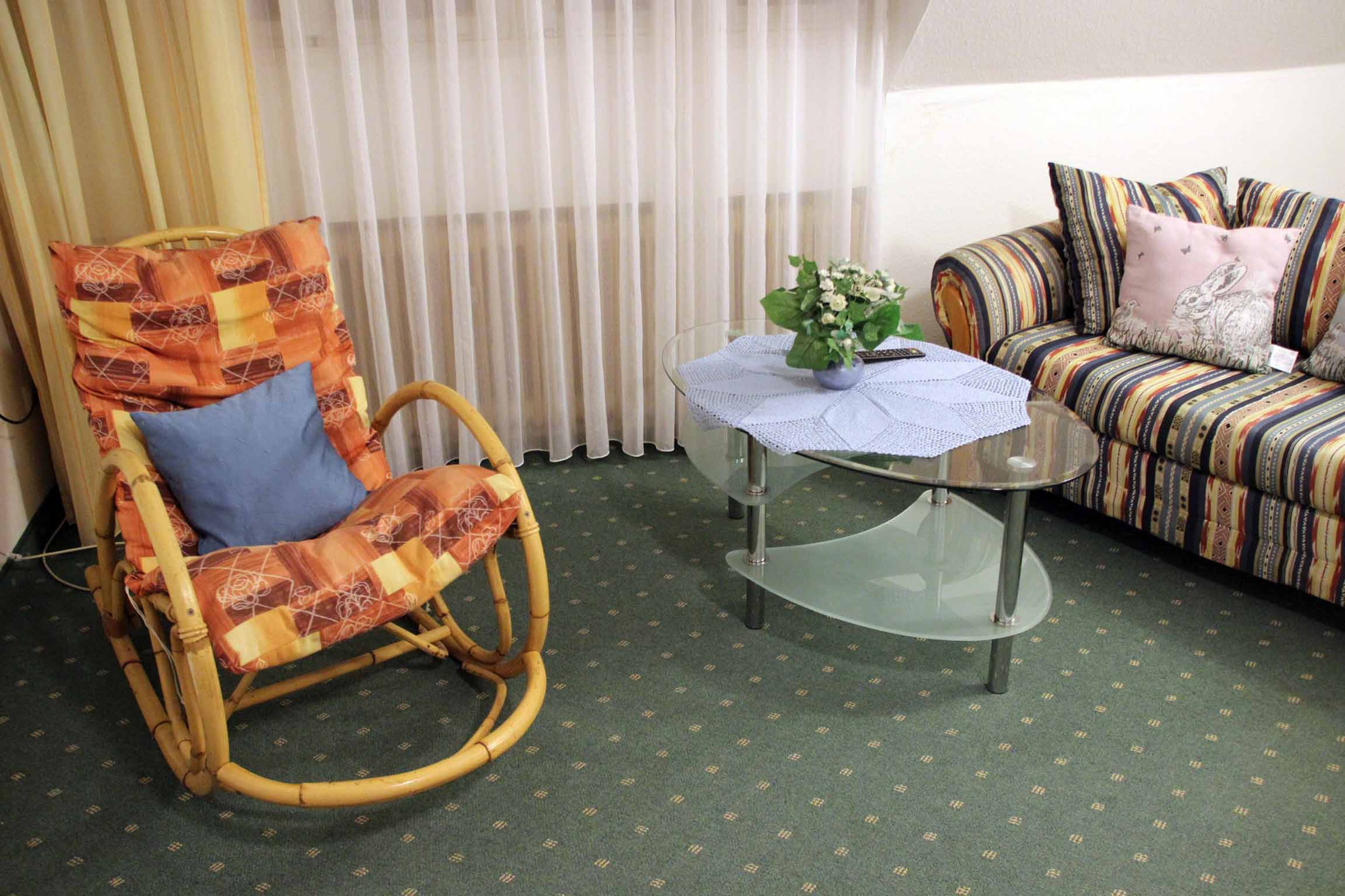 Una habitació amb una cadira d'oscill·lar de vimet, una taula de cafè de vidre amb un corredor de taula de renda i un sofà a ratlles amb coixins estampats.
