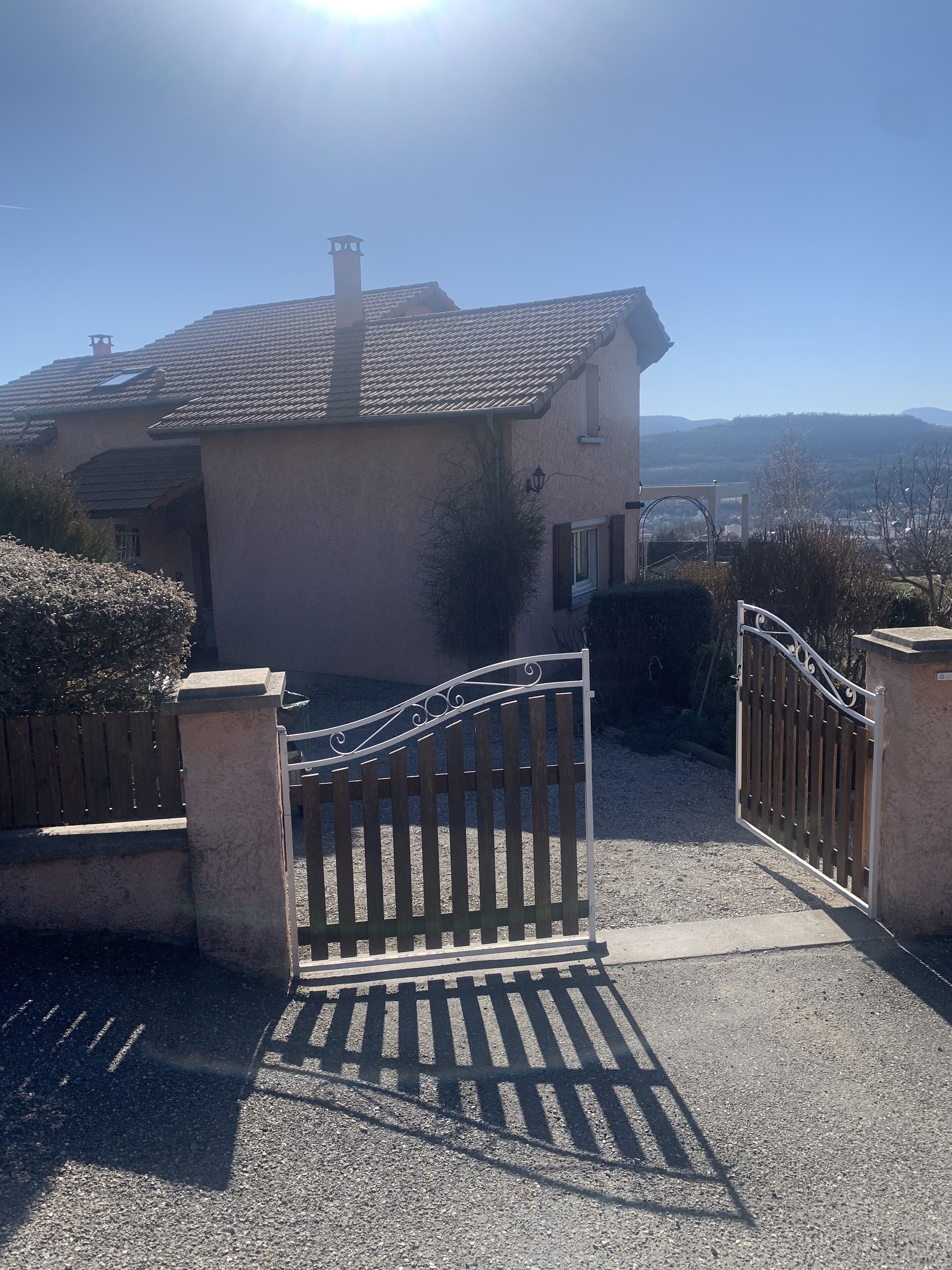 A house with a gated entrance, a driveway, and a view of distant hills.