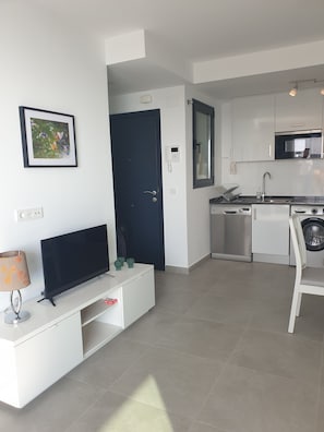 A modern kitchen with white cabinets, a microwave, and a dishwasher. There is a framed picture on the wall and a TV on a white cabinet.