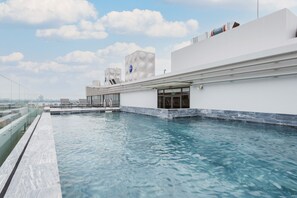 A rooftop infinity pool with a glass balustrade, a modern building with geometric design elements, and a clear sky. - Lexington Apartments - Westlake (Hanoi)