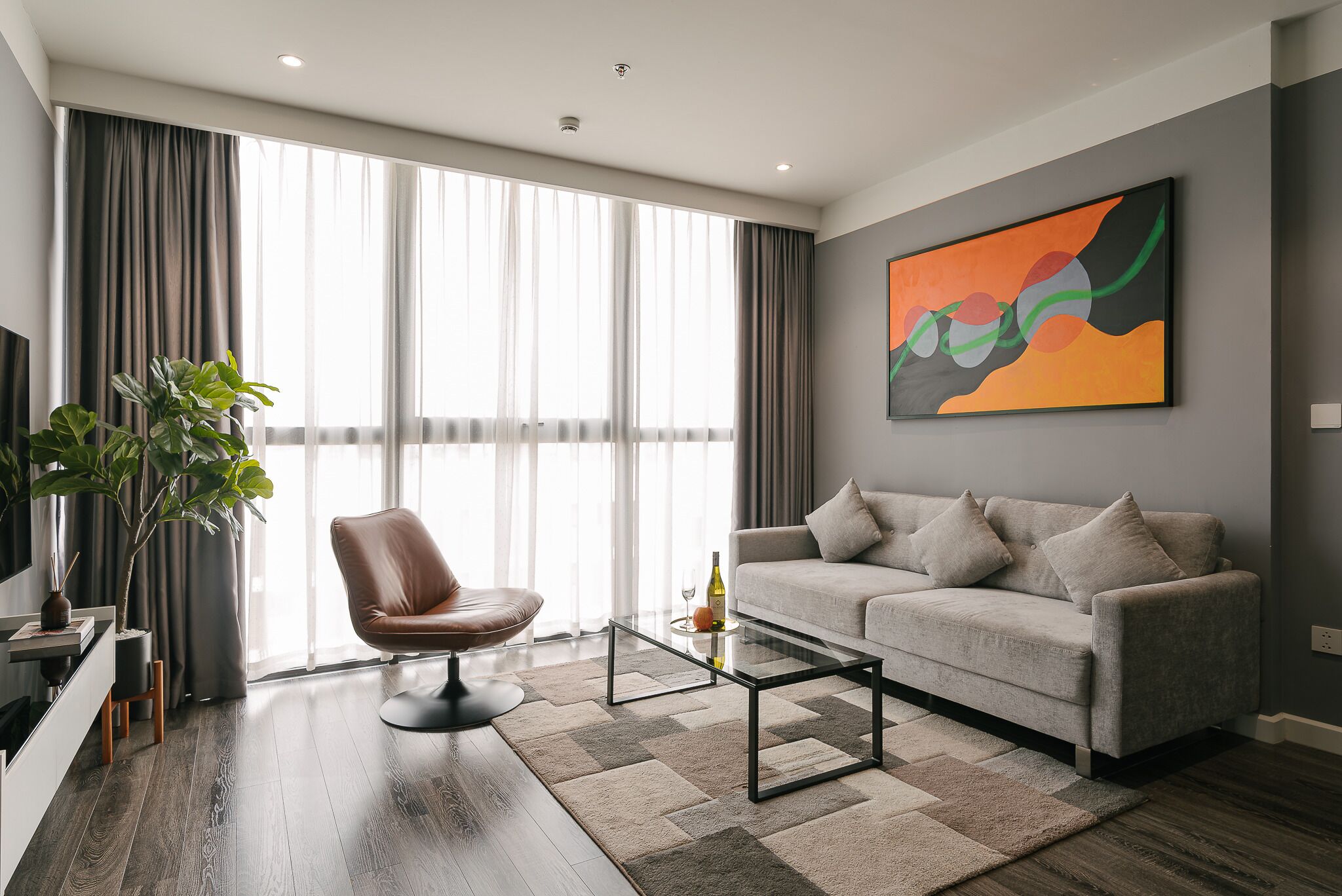 A modern living room with a sofa, a glass coffee table, and a brown leather chair.
