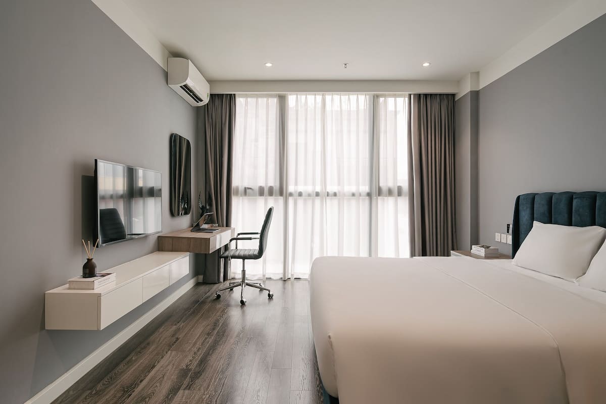 Ein modernes Hotelzimmer mit einem großen Bett, einem Schreibtisch mit Stuhl, einem Fernseher und einem Fenster mit Vorhängen.