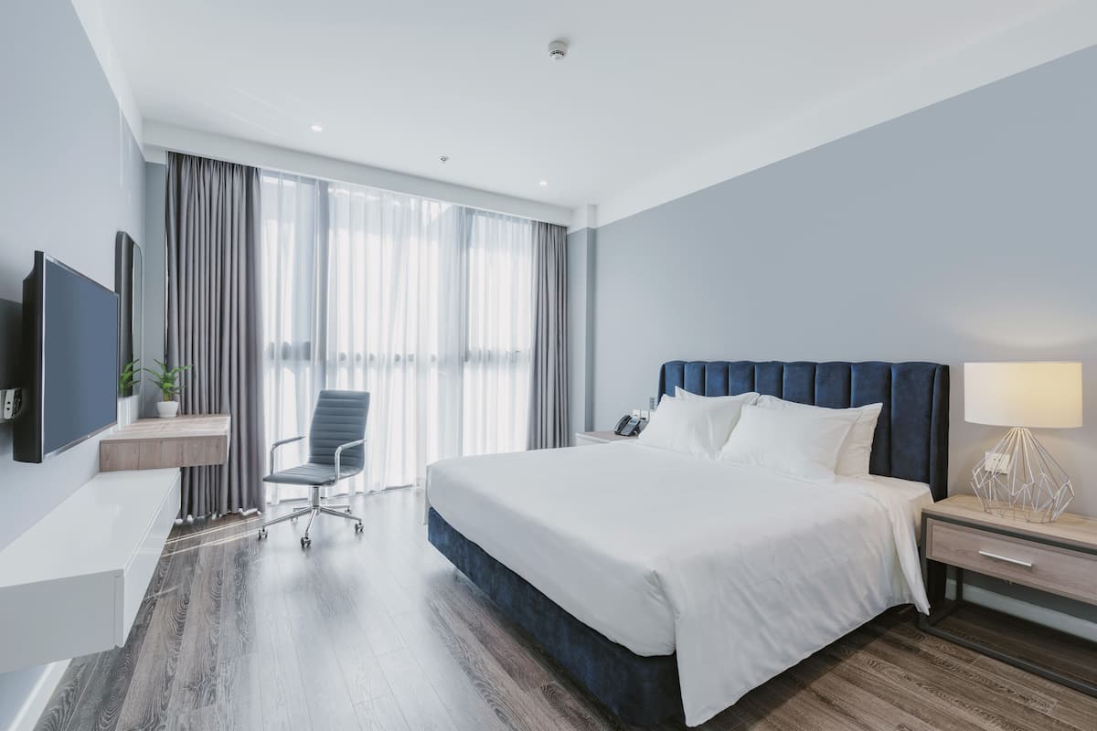Ein modernes Hotelzimmer mit einem großen Bett, einem Schreibtisch, einem Sessel, einem Fernseher und einem Fenster mit Vorhängen.