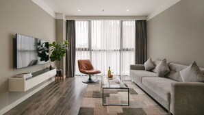 Ein modernes Wohnzimmer mit Flachbildfernseher, einer Couch, einem Couchtisch und einem Sessel.