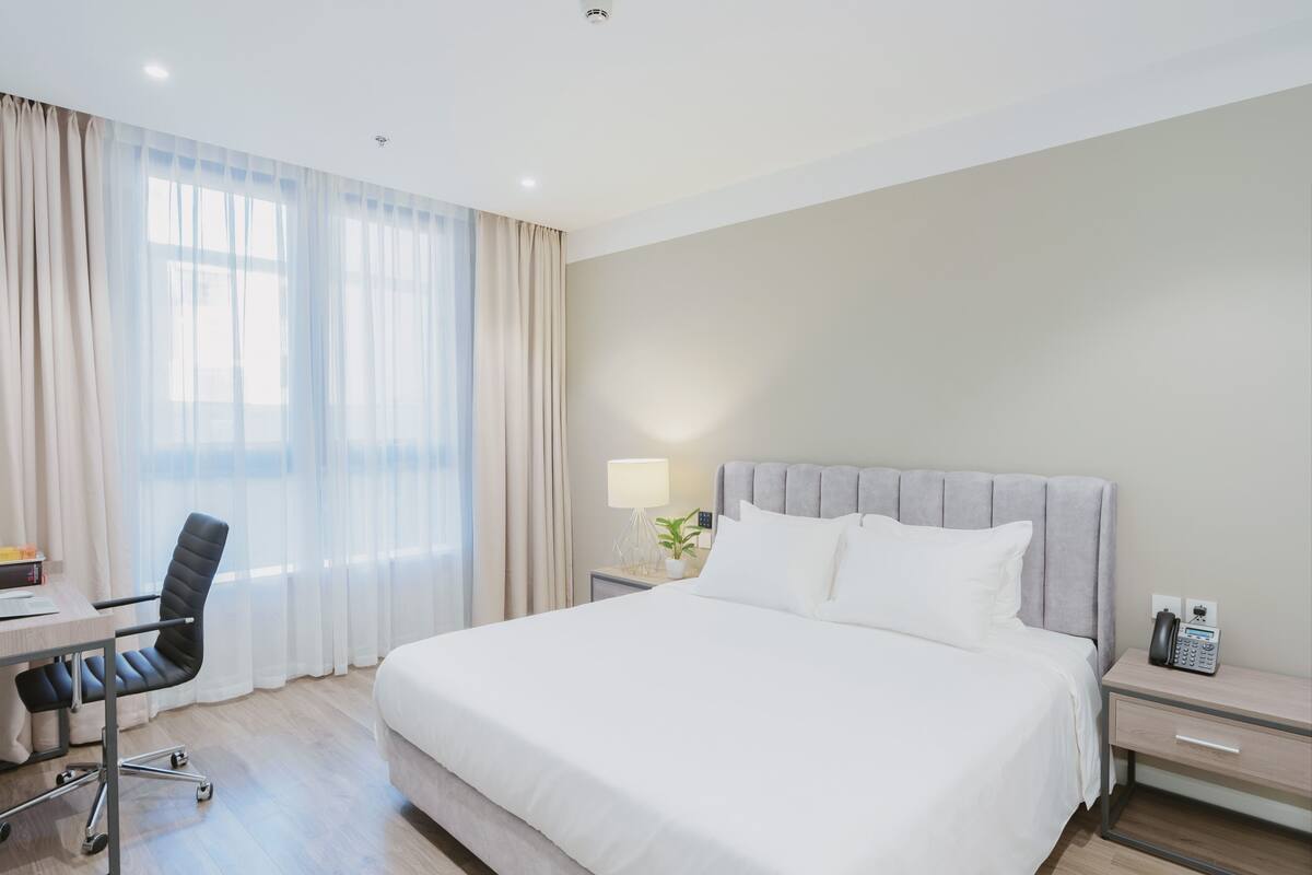 Ein Hotelzimmer mit Bett, Schreibtisch, Stuhl, Lampe und Telefon.