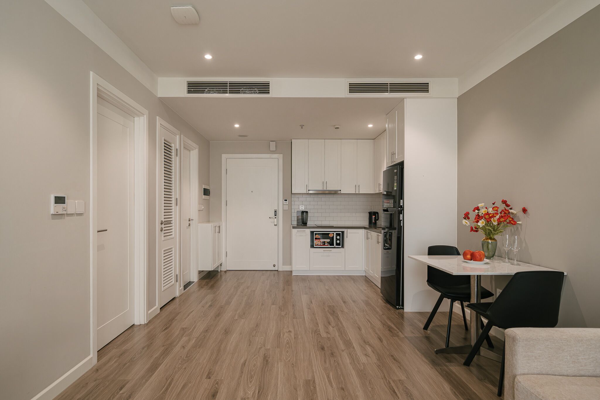 A modern kitchen with white cabinets, a black refrigerator, and a dining area with a table and chairs.