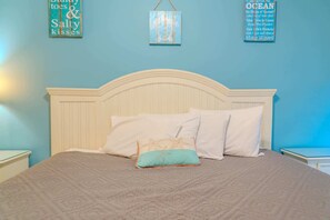 Una cama con cabecera blanca, dos almohadas blancas y una almohada azul verdosa con diseño de estrella de mar.