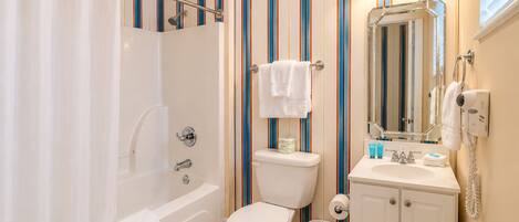 Ein Badezimmer mit Badewanne, Toilette und Waschbecken, ausgestattet mit Streifenmuster-Tapete und einem beleuchteten Spiegel.