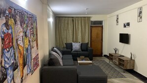 A living room with a dark grey sofa, a coffee table, and a painting on the wall. - Immaculate 2-bed Apartment, Langata, Nairobi (Nairobi)