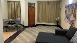 A living room with a sofa, a dining table with chairs, a door, and a painting on the wall. - Immaculate 2-bed Apartment, Langata, Nairobi (Nairobi)