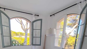 A bedroom with a bed, two windows, a radiator, and a view of trees.