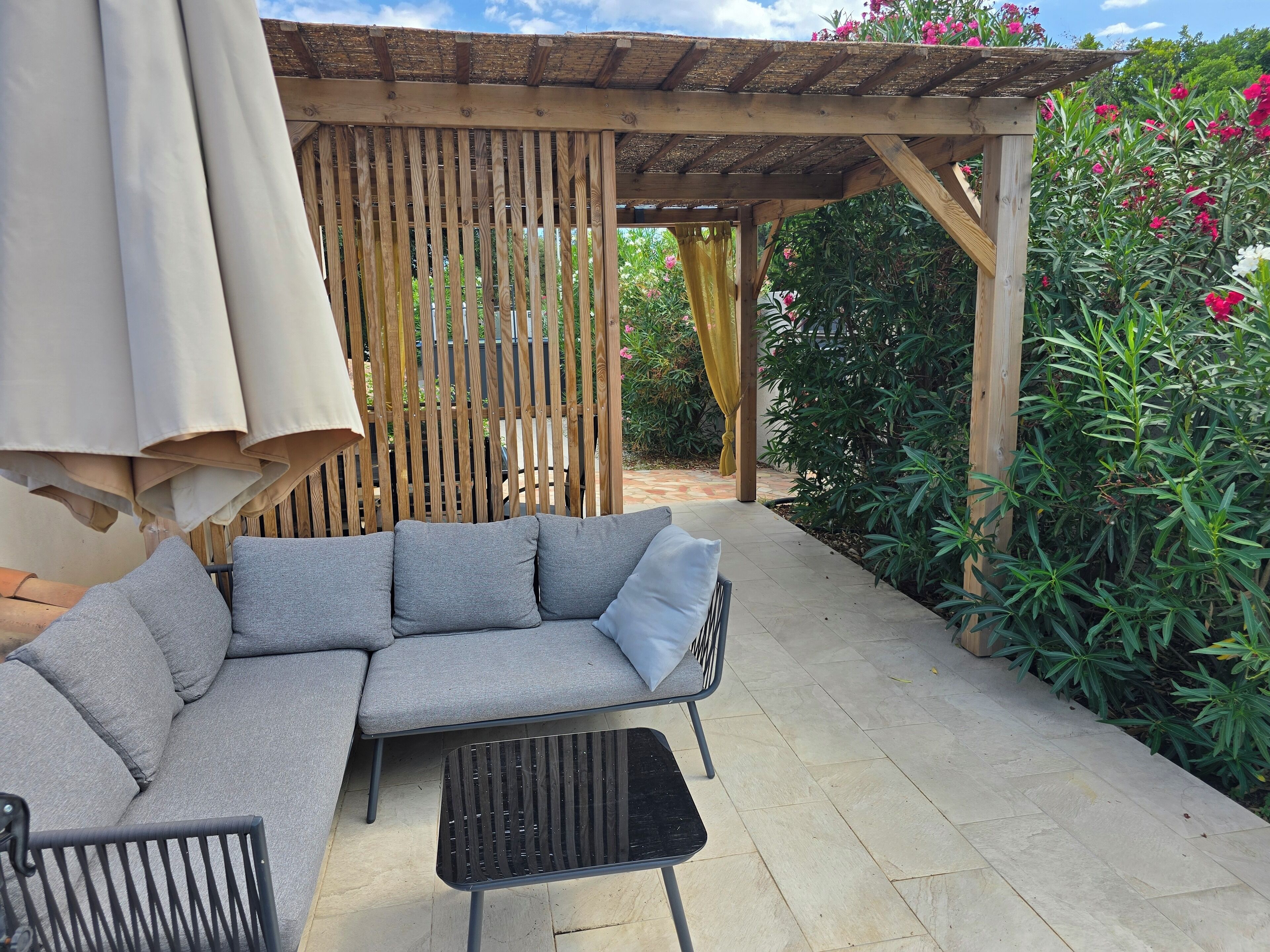 A covered outdoor seating area with a sofa and chairs, a table, and a pergola structure.