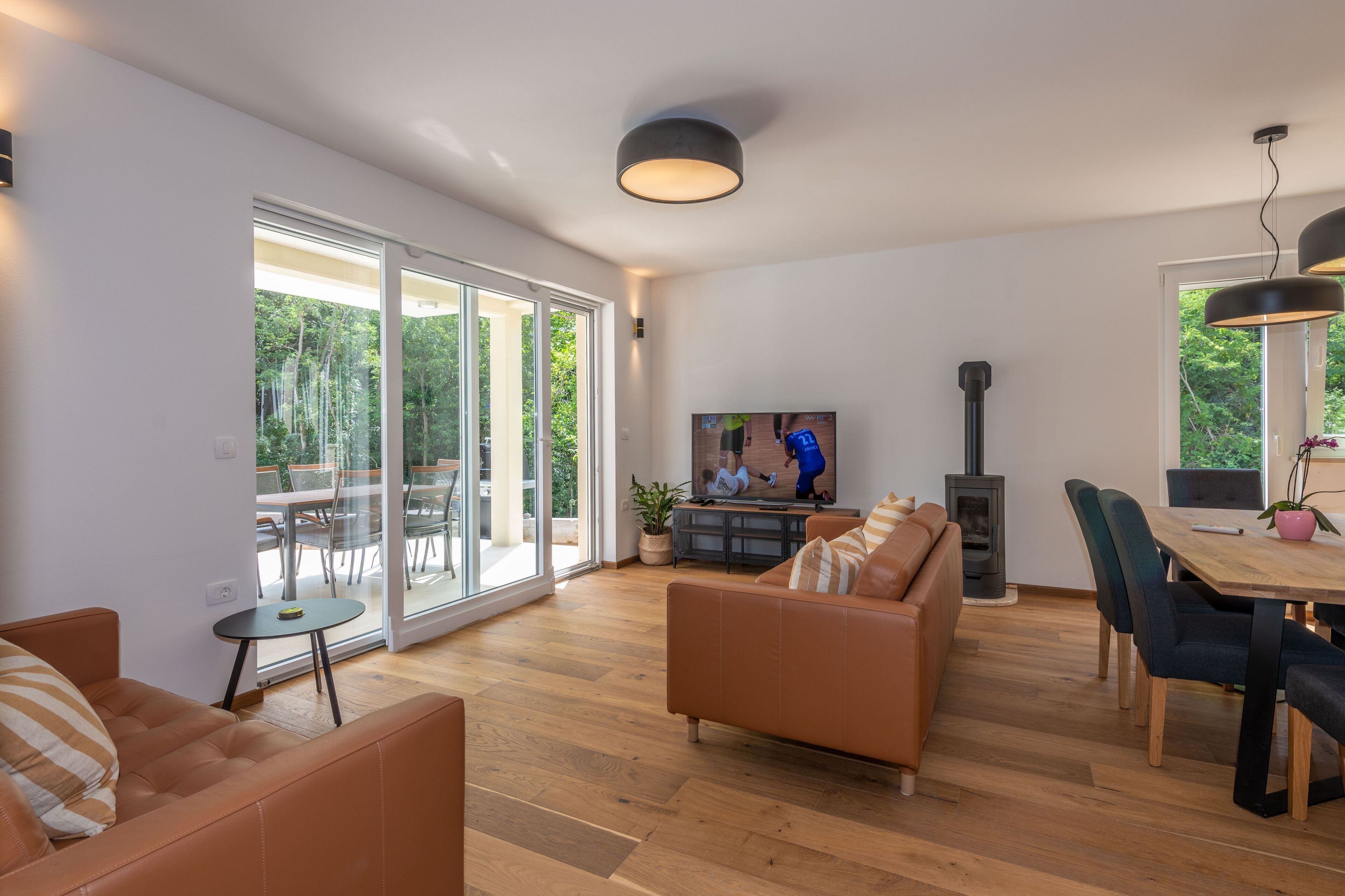 A spacious living room with a large sliding glass door leading to an outdoor area, a fireplace, and a dining table with chairs.