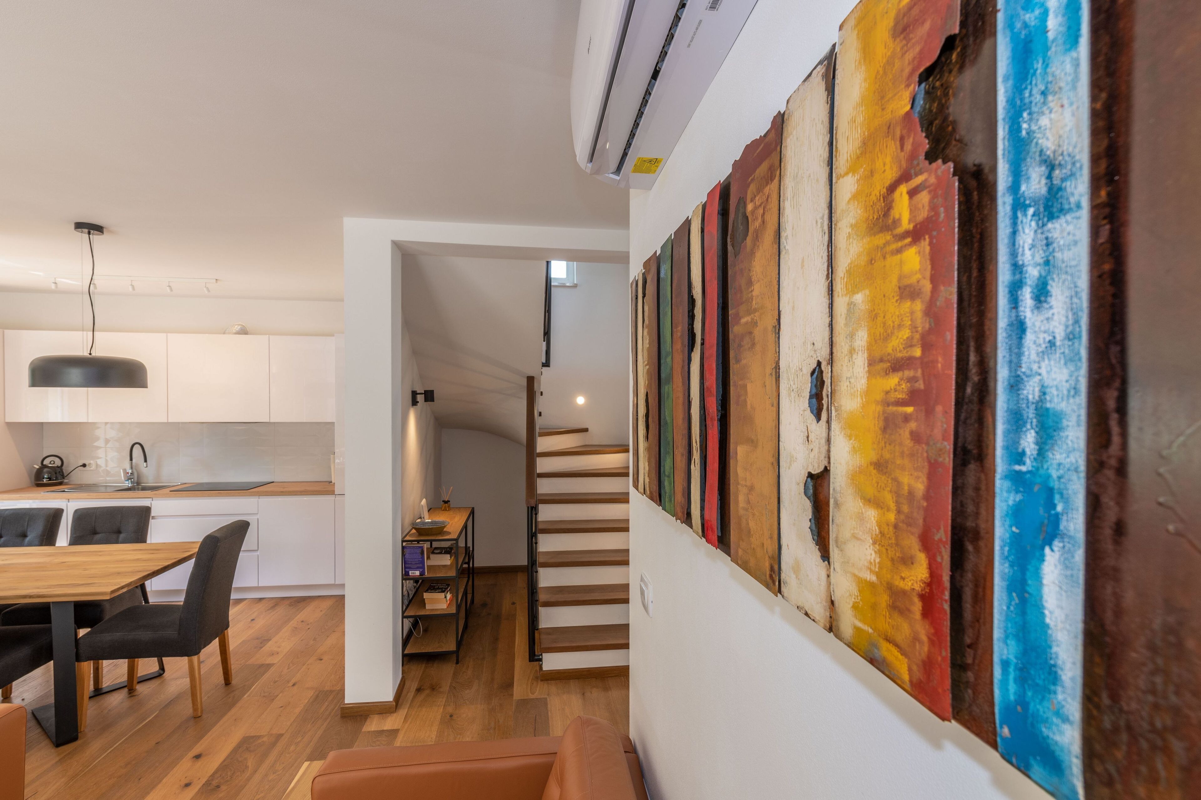 A modern kitchen with white cabinets, a wooden dining table, and a staircase leading to another level.