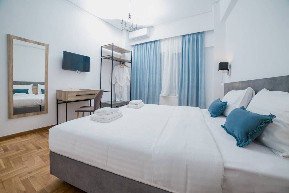 A hotel room with a bed, a desk, a chair, a mirror, a TV, and a wardrobe.