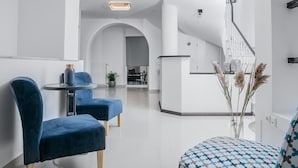 A modern hotel lobby with a reception desk, a seating area with blue upholstered chairs, and a patterned ottoman. - Acropolis Vision (Athens)