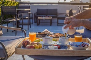 Een ontbijtkarretje met fruit, gebak, koffie en sap op een balkon.