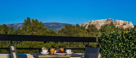 A terrace with a table set for a meal, overlooking a historic building and a mountainous landscape.