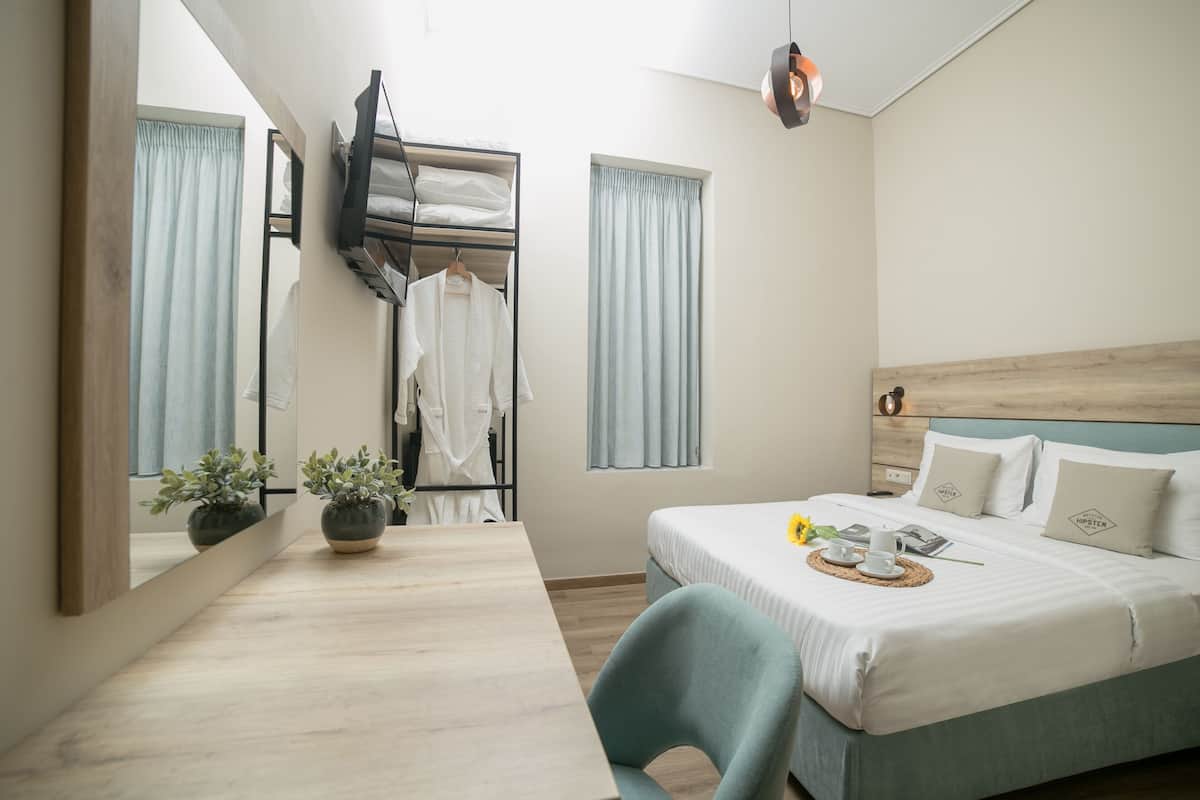 A hotel room with a bed, a desk, a mirror, a TV, and two windows with curtains.