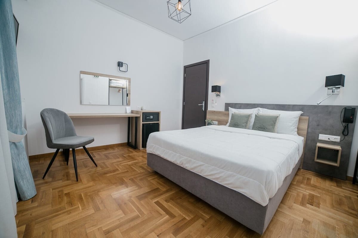 A bedroom with a bed, a desk, a chair, a wardrobe, and a small cabinet.