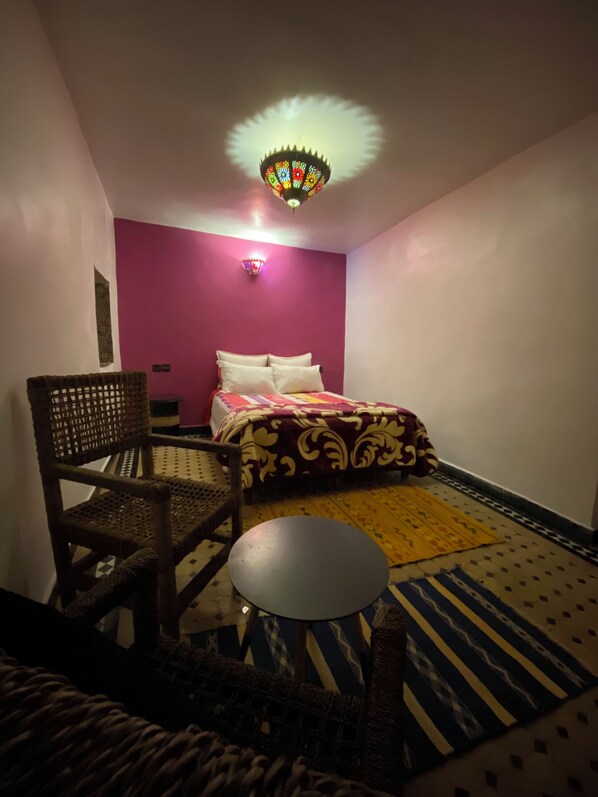A room with a bed, a chair, a small table, and a decorative ceiling light.