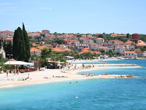 Eine Küstenstadt mit Strand, Häusern mit roten Dächern und einem klaren, blauen Himmel.