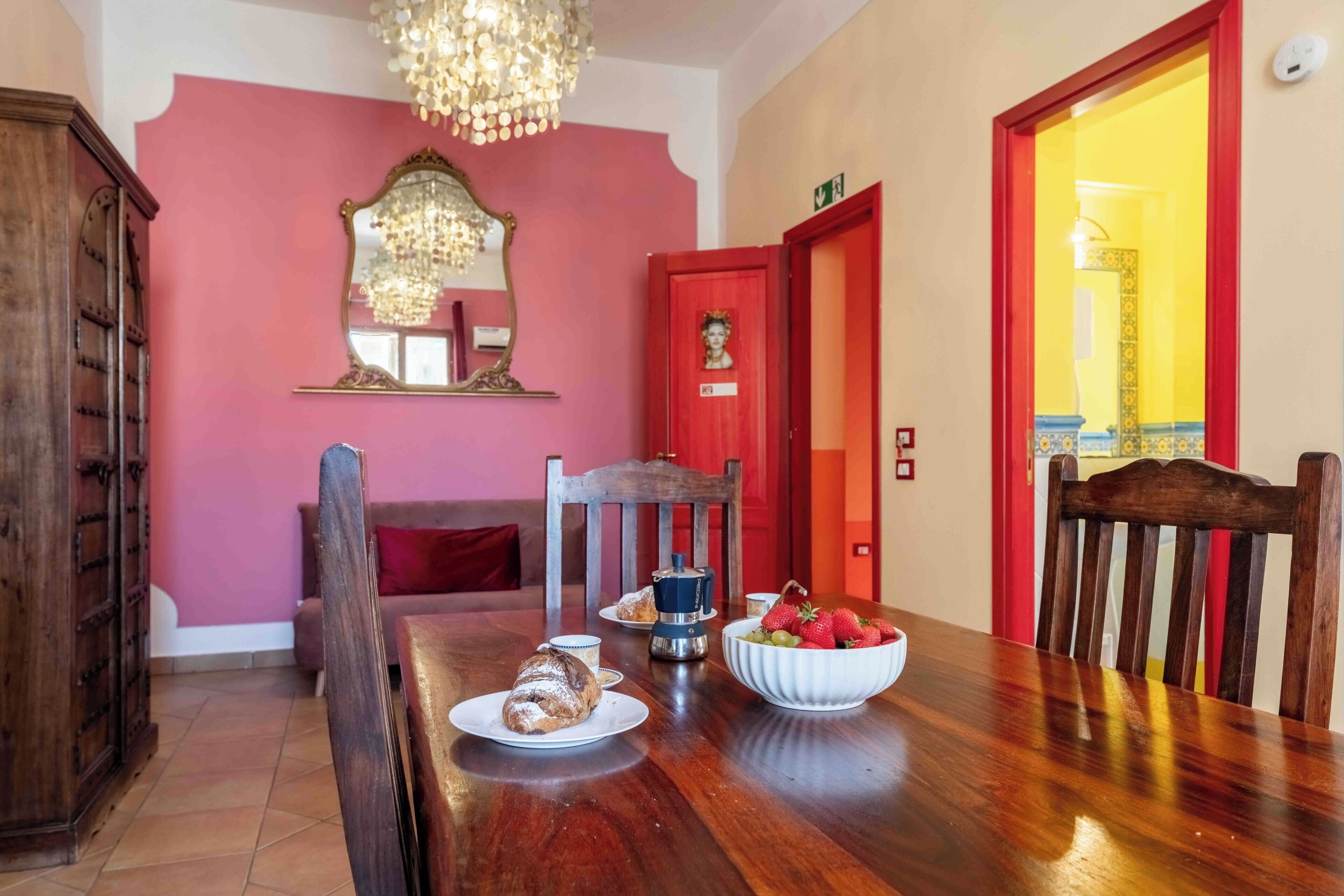 Un coin repas avec une table en bois, des chaises, un lustre et une porte rouge.