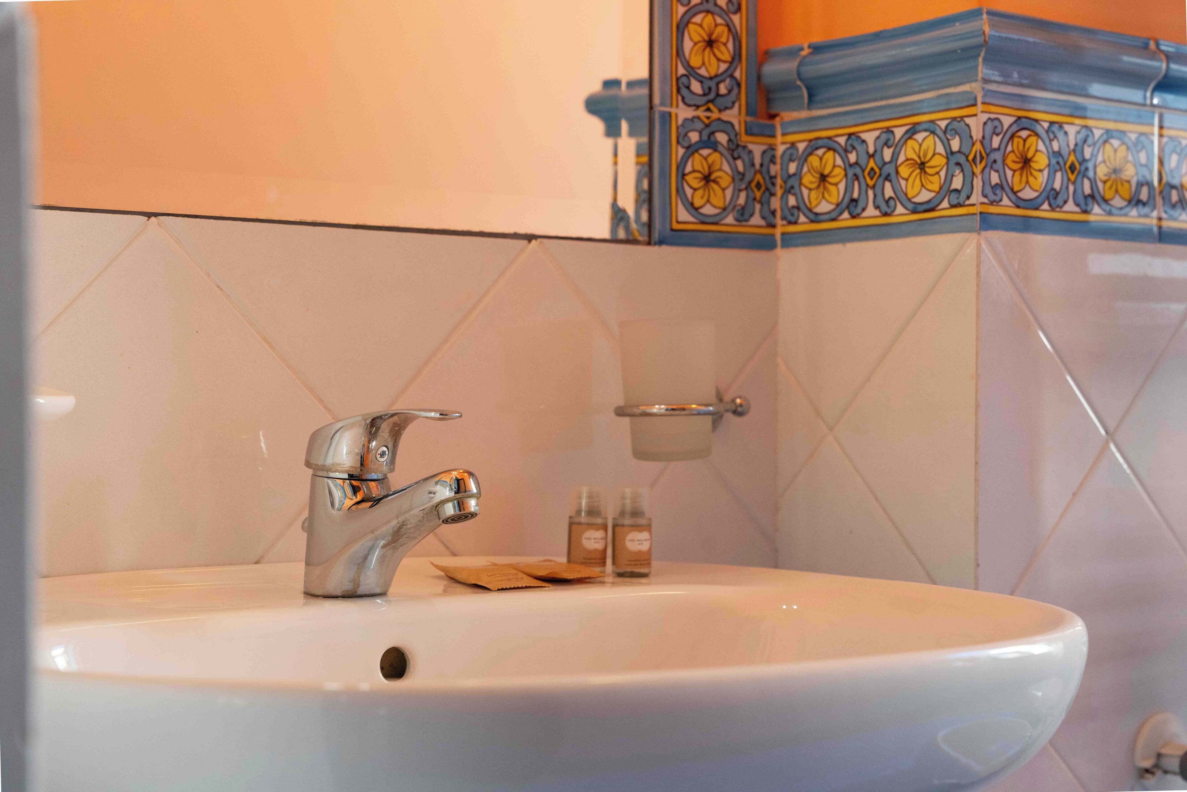 Un bagno con un lavandino bianco, un rubinetto cromato e piastrelle decorative al muro.