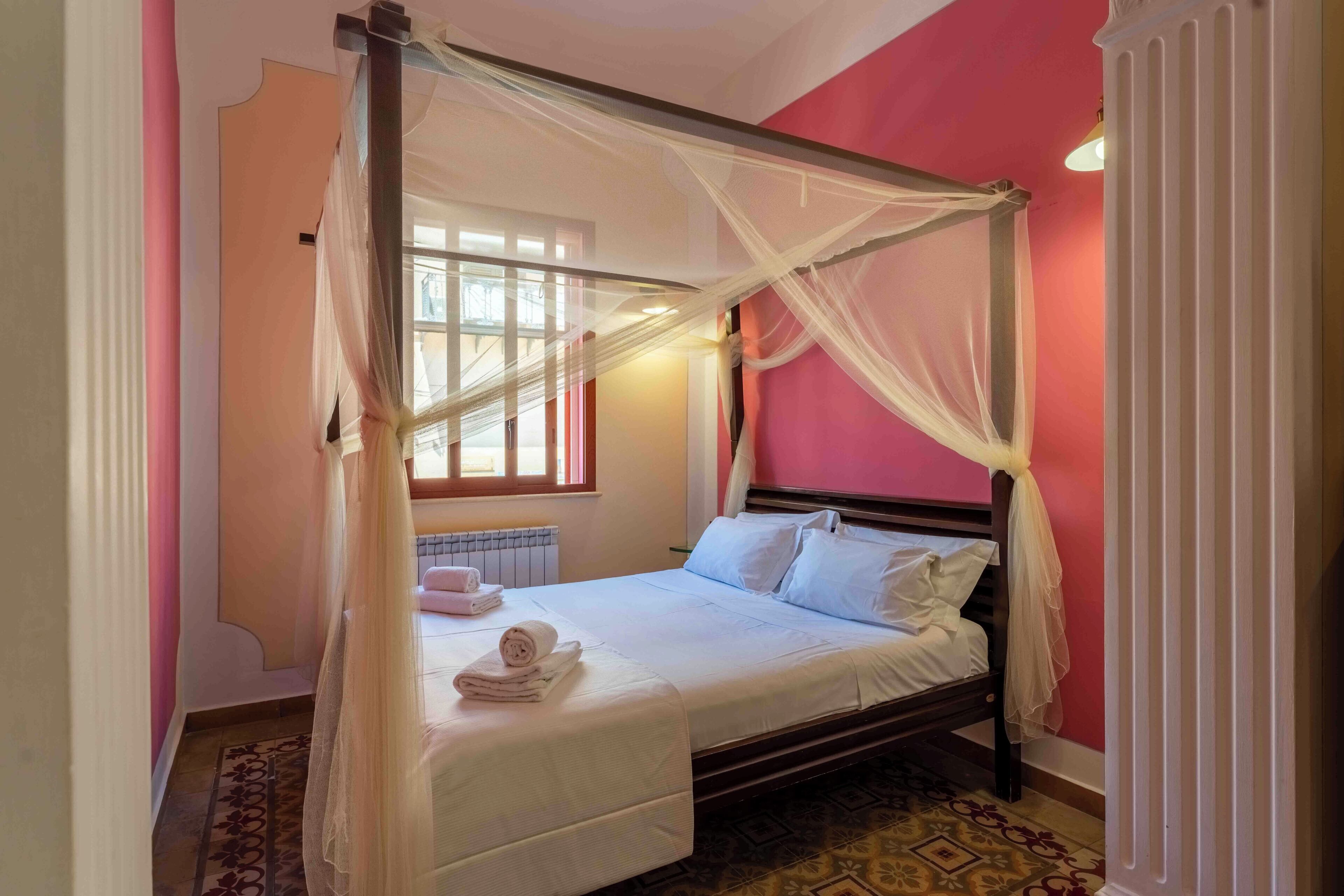A four-poster bed with white linens, a radiator, and a patterned rug.