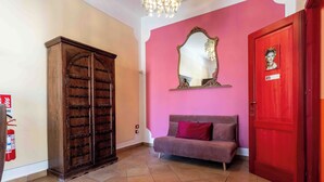 Una habitación con un armario de madera, una pared rosa, un espejo, una puerta roja y un sofá gris.