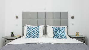 A neatly arranged bedroom with a grey upholstered headboard, two bedside tables with decorative items, and a grey quilted bedspread.