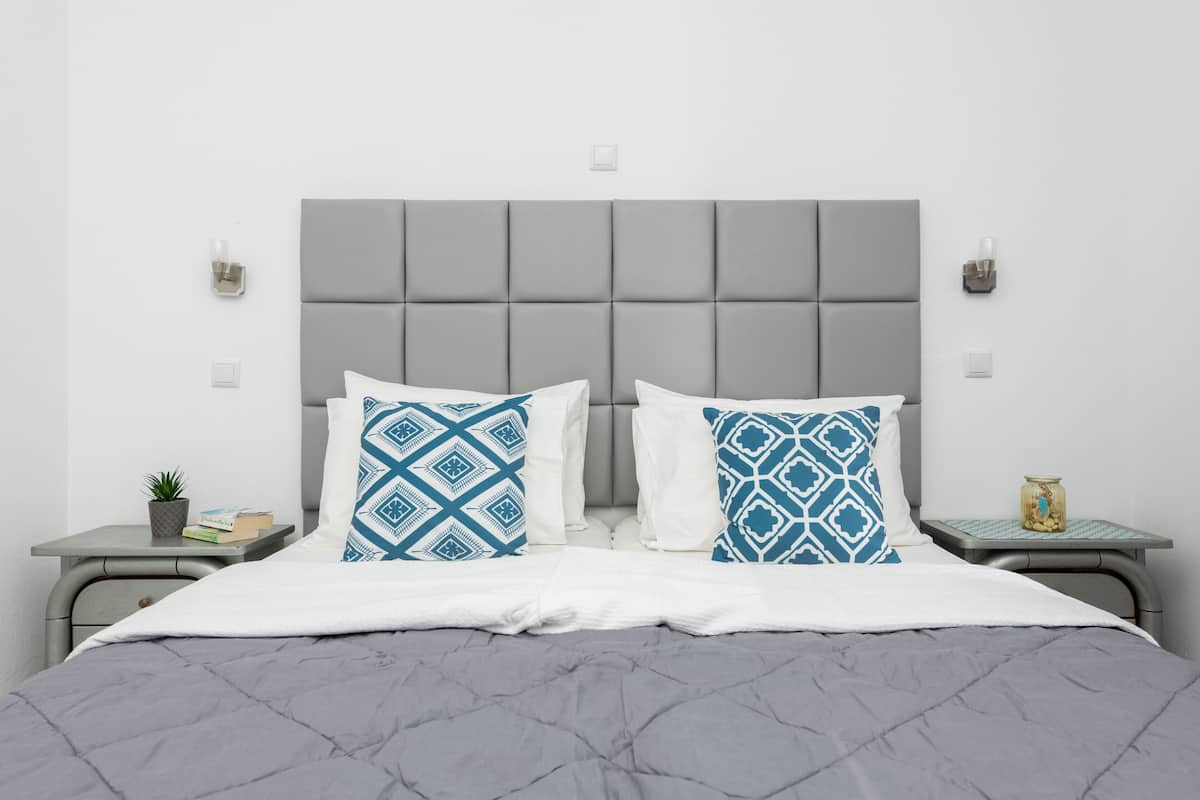 A neatly arranged bedroom with a grey upholstered headboard, two bedside tables with decorative items, and a grey quilted bedspread.